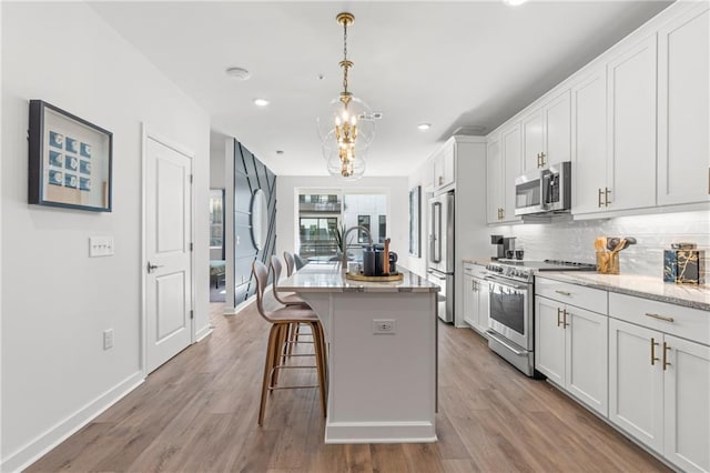 kitchen with a kitchen breakfast bar, light wood-type flooring, stainless steel appliances, and a kitchen island with sink