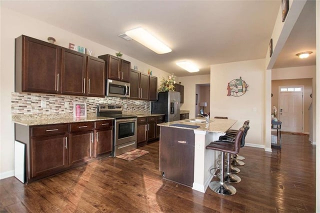 kitchen with backsplash, an island with sink, a breakfast bar, dark brown cabinets, and appliances with stainless steel finishes