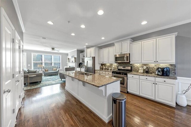 kitchen with stainless steel appliances, a kitchen breakfast bar, dark hardwood / wood-style flooring, a kitchen island with sink, and white cabinets