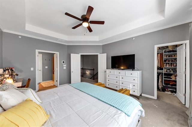 carpeted bedroom with ceiling fan, a spacious closet, a tray ceiling, and a closet