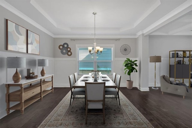 dining area with dark wood-type flooring, wainscoting, an inviting chandelier, and a raised ceiling