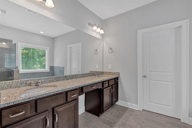 bathroom featuring visible vents, baseboards, a sink, a tile shower, and double vanity