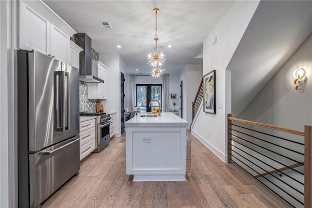 kitchen with white cabinetry, wall chimney exhaust hood, stainless steel appliances, light wood finished floors, and a sink