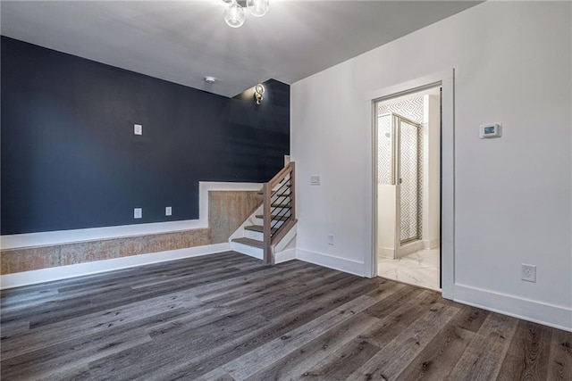spare room with stairway, dark wood-style flooring, and baseboards