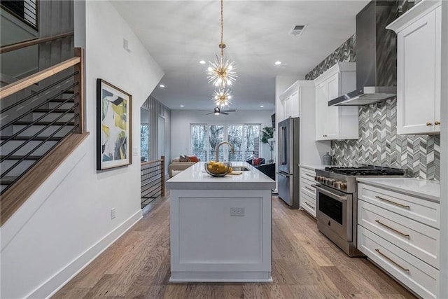 kitchen featuring wall chimney range hood, light wood-style flooring, backsplash, visible vents, and premium appliances