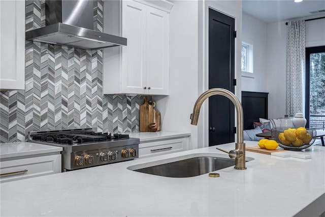 kitchen featuring white cabinets, wall chimney exhaust hood, a sink, stove, and decorative backsplash