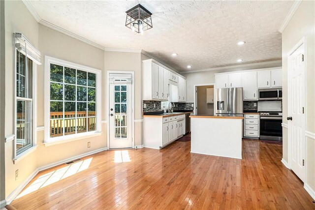 kitchen with crown molding, white cabinetry, wood-type flooring, and stainless steel appliances