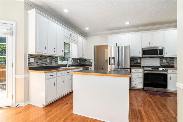 kitchen with stainless steel appliances, white cabinetry, sink, wood-type flooring, and tasteful backsplash