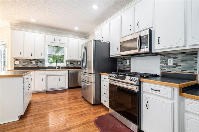 kitchen with backsplash, light hardwood / wood-style floors, stainless steel appliances, ornamental molding, and white cabinets