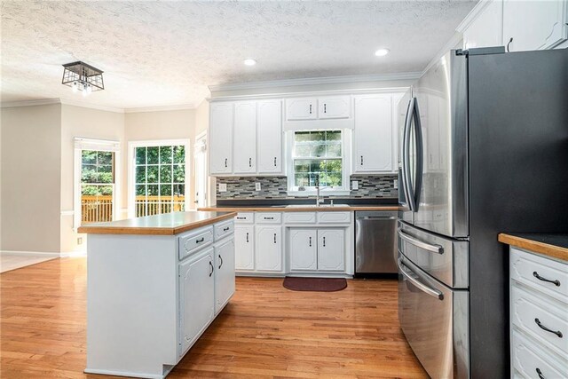 kitchen with ornamental molding, light hardwood / wood-style flooring, backsplash, stainless steel appliances, and white cabinets