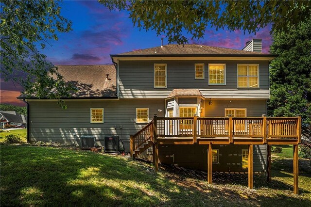 back house at dusk featuring a deck, a lawn, and central AC