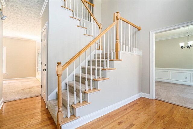 staircase featuring ornamental molding, a textured ceiling, hardwood / wood-style flooring, and a chandelier