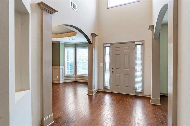 foyer entrance featuring visible vents, crown molding, arched walkways, baseboards, and dark wood-type flooring