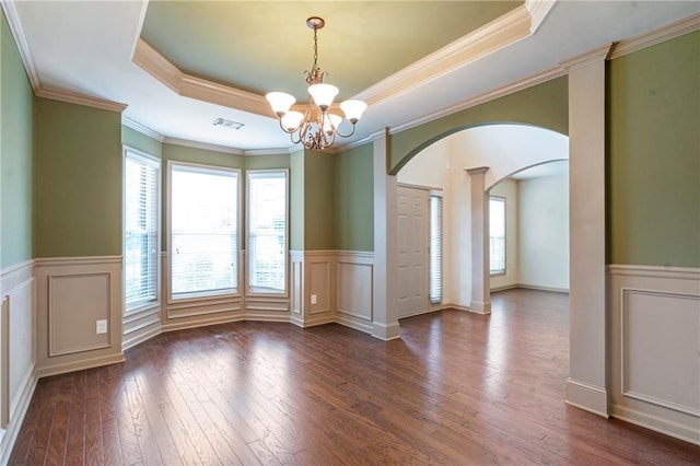 unfurnished dining area with arched walkways, a tray ceiling, a healthy amount of sunlight, and hardwood / wood-style flooring