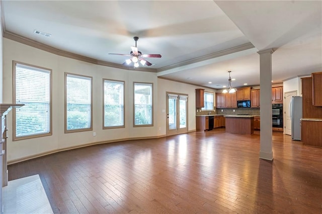 unfurnished living room with decorative columns, ornamental molding, ceiling fan with notable chandelier, and dark wood-type flooring