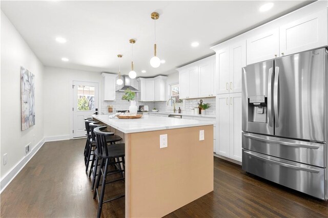 kitchen with a kitchen breakfast bar, stainless steel refrigerator with ice dispenser, a center island, dark wood finished floors, and backsplash