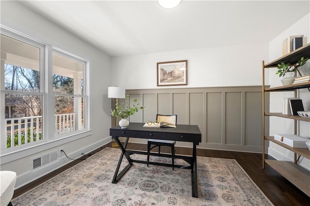 office featuring a wealth of natural light, visible vents, a decorative wall, and dark wood-style flooring