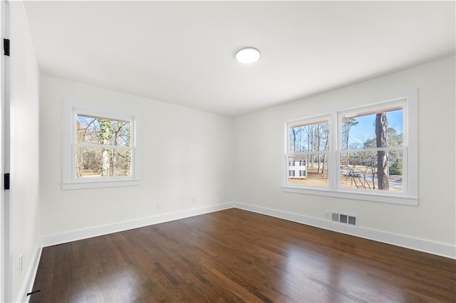 empty room with baseboards, visible vents, and dark wood-type flooring