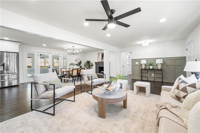 living room featuring ceiling fan with notable chandelier, a fireplace, wood finished floors, and recessed lighting