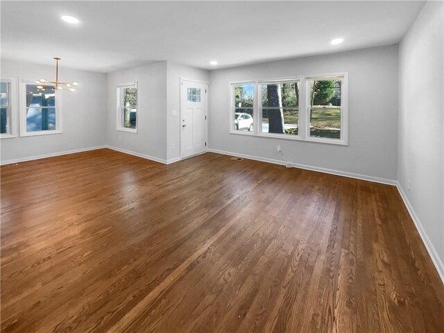 unfurnished living room with plenty of natural light, dark hardwood / wood-style flooring, and an inviting chandelier