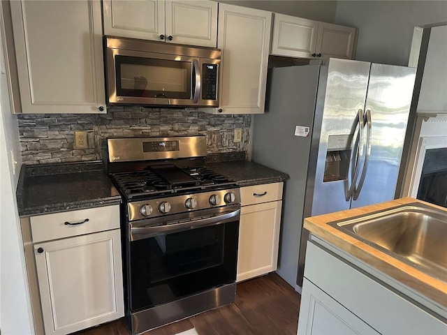 kitchen with a sink, dark wood-type flooring, appliances with stainless steel finishes, white cabinetry, and tasteful backsplash