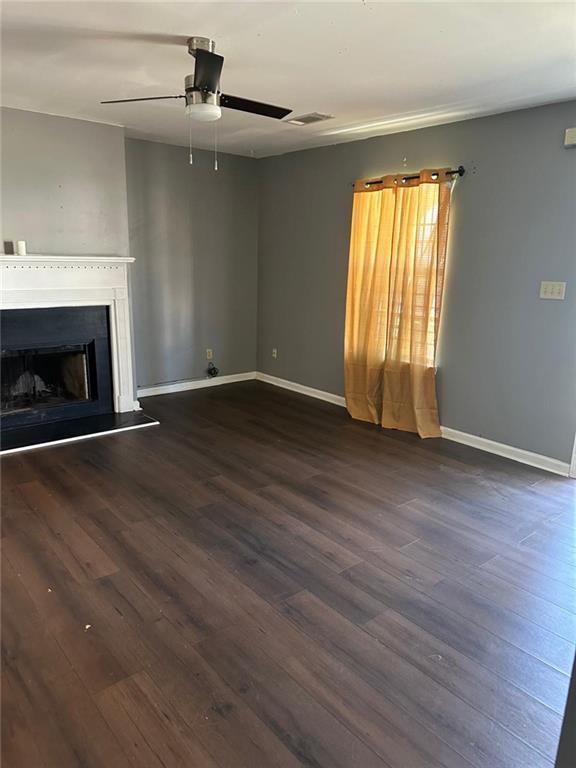 unfurnished living room featuring visible vents, baseboards, dark wood-type flooring, and a fireplace with raised hearth