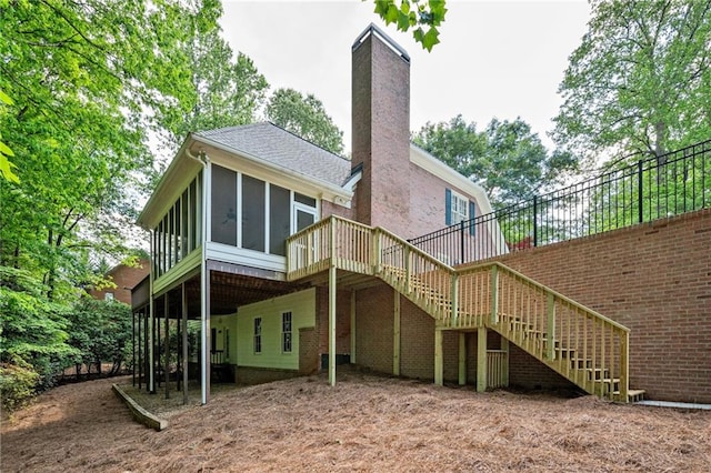 rear view of property featuring a sunroom, a chimney, stairway, and a deck