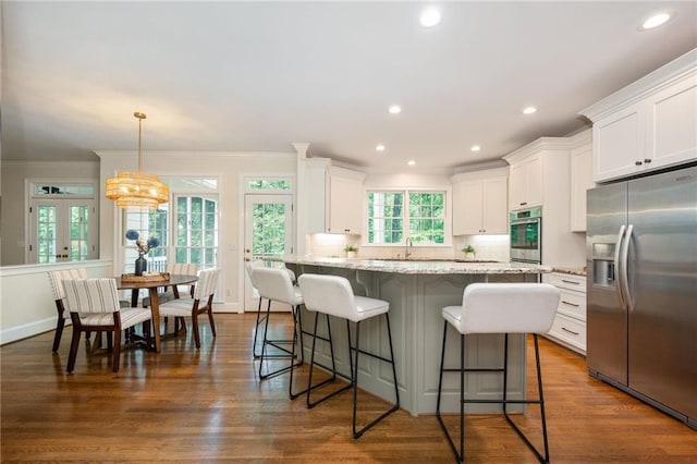 kitchen with a breakfast bar area, light stone counters, white cabinets, ornamental molding, and stainless steel appliances