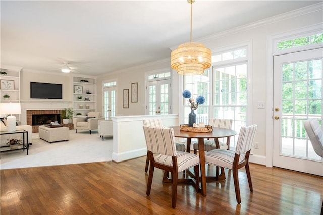 dining room with ornamental molding, ceiling fan with notable chandelier, wood finished floors, and built in shelves