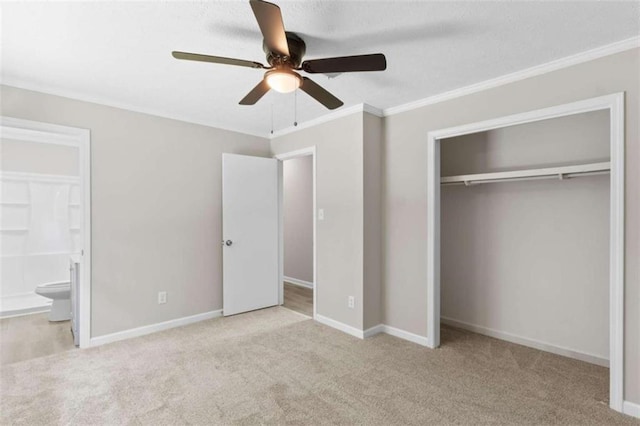 unfurnished bedroom with carpet, a closet, ensuite bathroom, crown molding, and ceiling fan