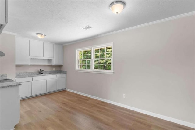 kitchen with ornamental molding, a textured ceiling, baseboards, light wood finished floors, and white cabinetry