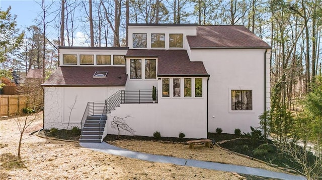 view of front of house with stucco siding, a shingled roof, and fence