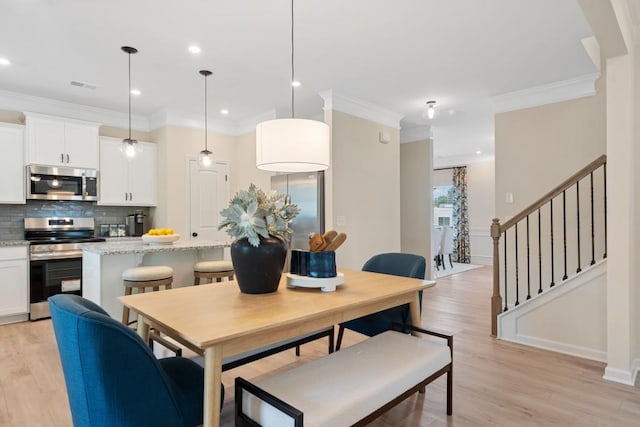 dining space with ornamental molding, light wood-style flooring, and stairs