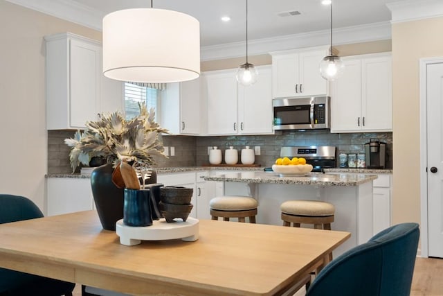 kitchen featuring visible vents, white cabinets, appliances with stainless steel finishes, a center island, and crown molding