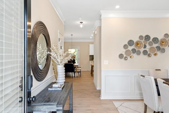 entrance foyer with light wood finished floors, ornamental molding, a decorative wall, and a wainscoted wall