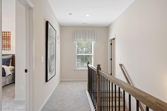 corridor with baseboards, an upstairs landing, and light colored carpet