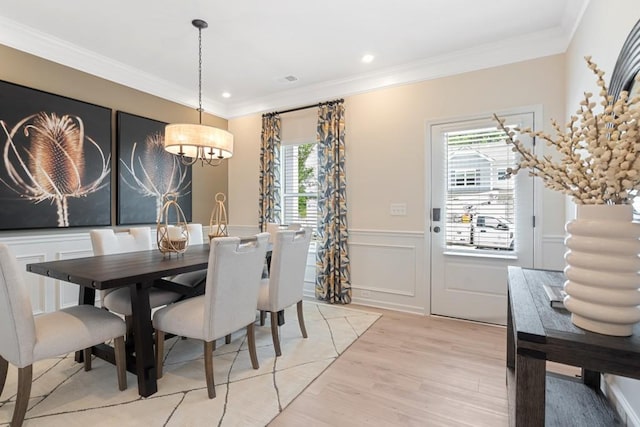 dining room featuring crown molding, recessed lighting, a decorative wall, light wood-style flooring, and wainscoting