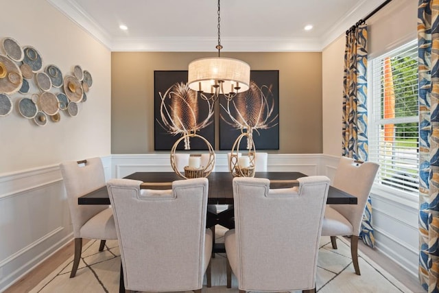 dining area with wainscoting, crown molding, light wood finished floors, and an inviting chandelier