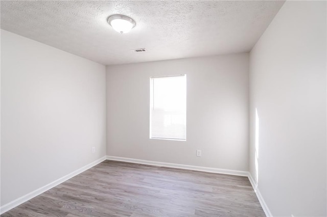 empty room with a textured ceiling, wood finished floors, visible vents, and baseboards