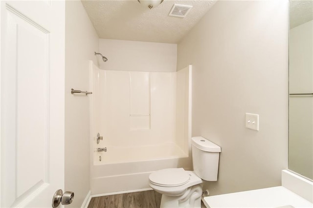 full bath with visible vents, toilet, a textured ceiling, wood finished floors, and bathing tub / shower combination