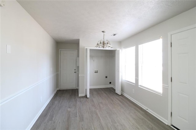 unfurnished dining area featuring light wood-type flooring, plenty of natural light, a notable chandelier, and baseboards