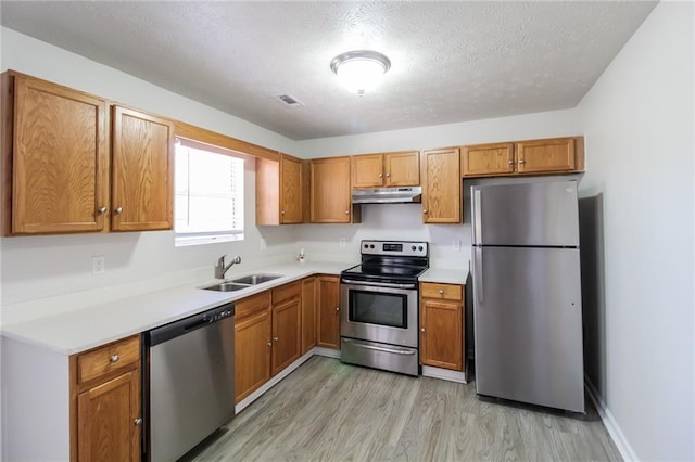 kitchen with visible vents, under cabinet range hood, light countertops, stainless steel appliances, and a sink