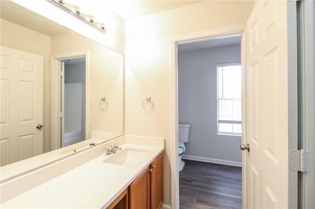 half bathroom with baseboards, toilet, wood finished floors, and vanity