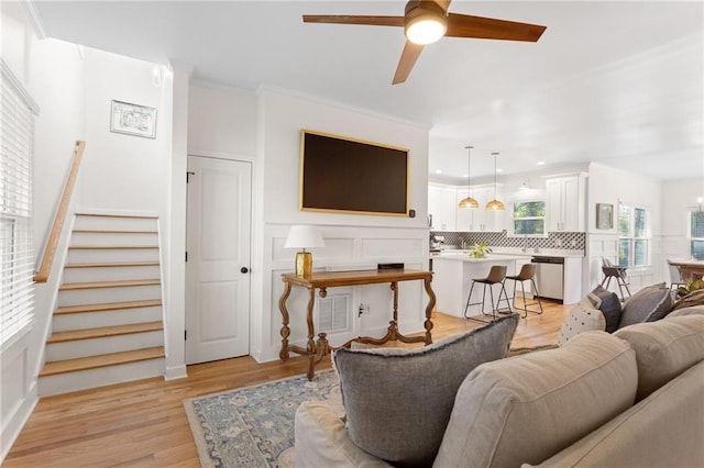 living room with ornamental molding, ceiling fan, and light wood-type flooring