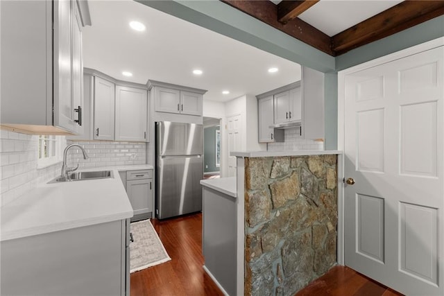 kitchen featuring sink, dark hardwood / wood-style flooring, beamed ceiling, and stainless steel refrigerator