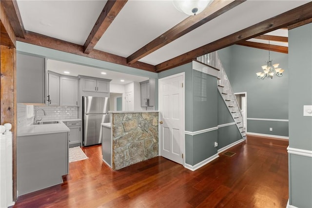 kitchen with stainless steel fridge, backsplash, dark wood-type flooring, a chandelier, and sink