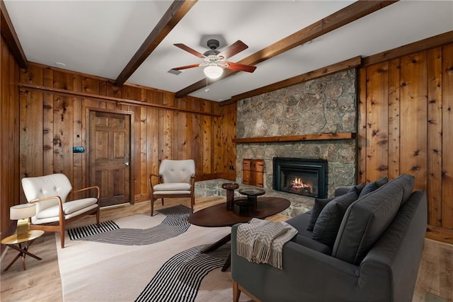 living area with wooden walls, a fireplace, ceiling fan, light hardwood / wood-style flooring, and beam ceiling