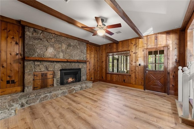 unfurnished living room featuring wood walls, ceiling fan, light wood-type flooring, a fireplace, and beamed ceiling