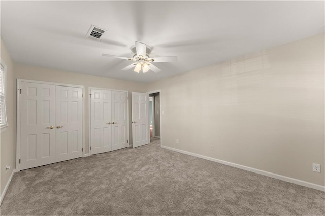 unfurnished bedroom featuring ceiling fan, light colored carpet, and multiple closets