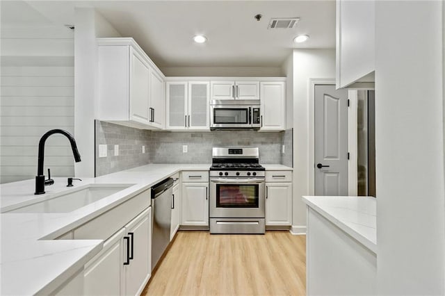 kitchen featuring white cabinetry, sink, light stone counters, light hardwood / wood-style floors, and appliances with stainless steel finishes